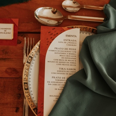 Prato decorativo com talheres, guardanapo verde e ementa em papel sobre mesa de madeira.