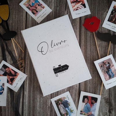 Livro branco com texto a preto rodeado por fotografias polaroid e adereços fotográficos sobre madeira