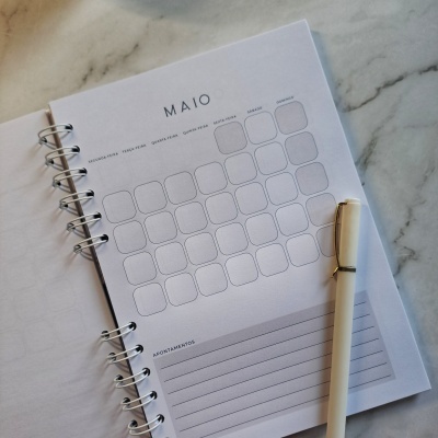 Agenda mensal de papel com calendário de maio e caneta branca sobre mármore
