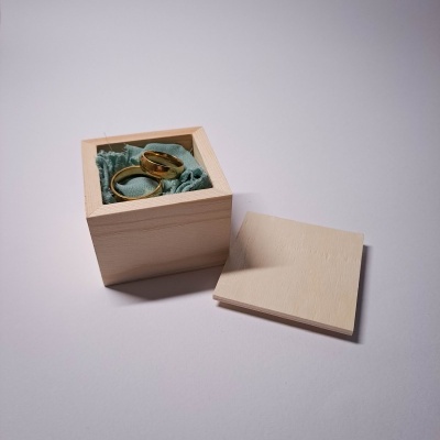 Caixa de madeira clara com duas alianças douradas e tecido azul esverdeado