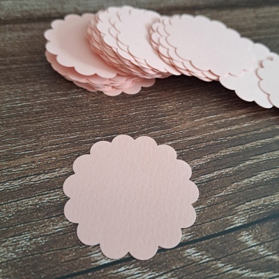 Peças de papel rosa claro em forma circular com bordas onduladas sobre madeira escura
