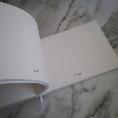 Livro aberto com páginas em branco e letras 'C&H' preto no canto inferior