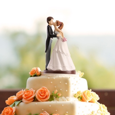 Bolo de casamento com figuras de noivo e noiva no topo e flores cor de pêssego decorativas