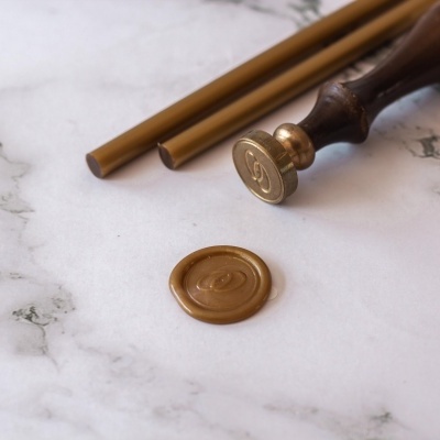 Materiais para lacre de cera dourada com carimbo e selo de cera sobre superfície marmoreada