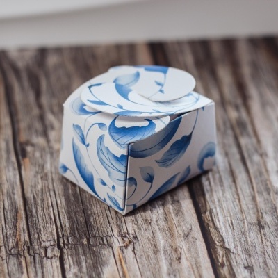 Caixa pequena de papel com padrão azul e branco de folhas e flores sobre superfície de madeira