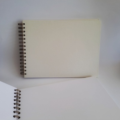 Dois cadernos de espiral creme, um aberto e outro fechado, sobre superfície branca