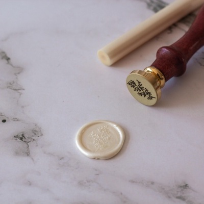 Carimbo de lacre com cabo de madeira e selo de cera branca numa superfície de mármore.