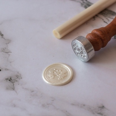 Selo de cera branco com carimbo de metal e cabo de madeira numa superfície de mármore