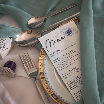 Mesa posta com prato decorativo azul e dourado, utensílios de metal e menu impresso ao lado