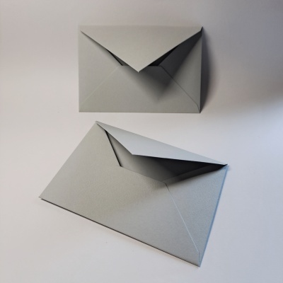 Dois envelopes cinza, um fechado e outro semiaberto, sobre superfície branca.