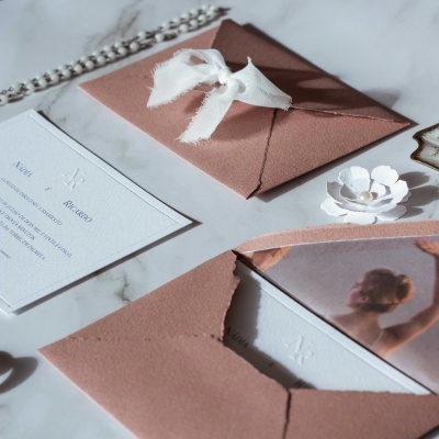 Convites de casamento com envelopes rosas e laços brancos sobre superfície marmoreada