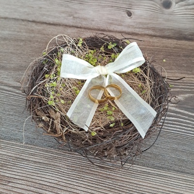 Cesta redonda com ramos secos, plantas verdes, fita branca e dois anéis dourados sobre madeira