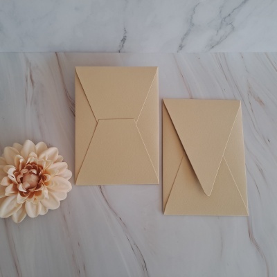 Duas envelopes bege sobre superfície marmoreada com flor decorativa