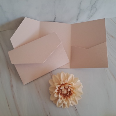 Envelope rosa claro com flor artificial numa superfície de mármore branco.