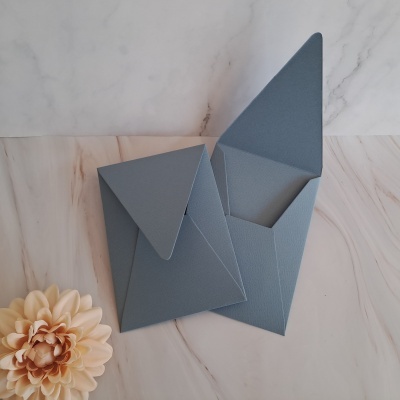 Cinco envelopes azuis com textura e uma flor artificial bege sobre superfície de mármore