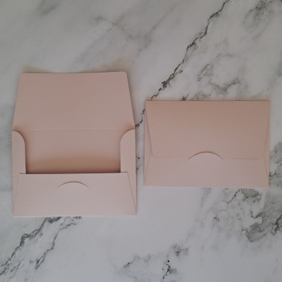 Dois envelopes cor-de-rosa claro, um aberto e um fechado, sobre mármore branco com veios cinzentos.