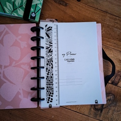 Planeador ou agenda rosa com padrão de folhas aberta, marcador transparente com padrão preto, sobre mesa de madeira