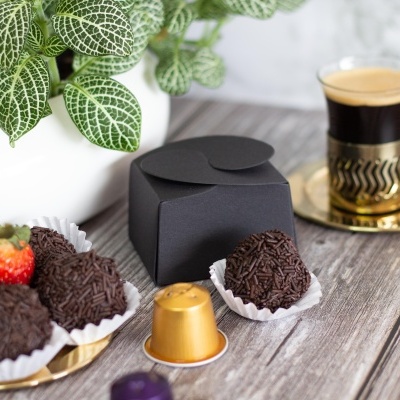 Trufas de chocolate, cápsulas de café, chávena de café e planta em vaso branco sobre mesa de madeira