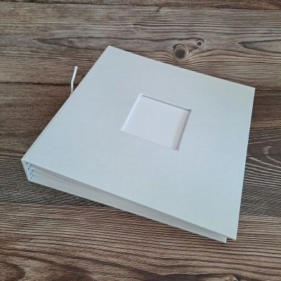 Álbum de fotografias branco quadrado com janela na capa sobre madeira clara