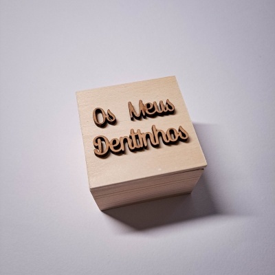 Caixa de madeira clara com texto 'Os Meus Dentinhas' em letras de madeira escuras na tampa