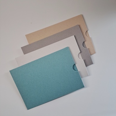 Quatro envelopes de cartão reciclado em azul, branco, cinza e bege sobre superfície branca