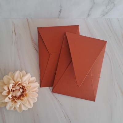 Dois envelopes terracota e uma flor creme sobre mármore branco