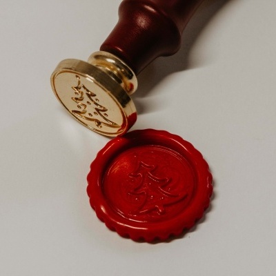 Selo de cera vermelho com carimbo dourado em suporte de madeira.