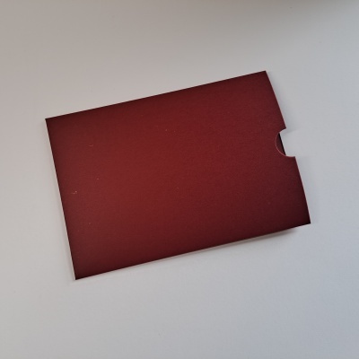 Envelope bordô liso com recorte semicircular sobre superfície branca