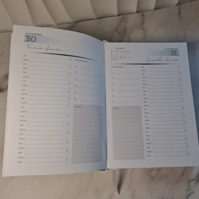 Página aberta de agenda diária nas datas 30 e 31 de dezembro sobre superfície de mármore com capa acolchoada cinza