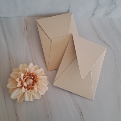 Dois envelopes bege claro com textura sobre superfície marmoreada com flor artificial creme