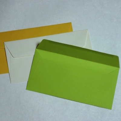 Três envelopes coloridos em papel, verde, branco e amarelo, sobre superfície branca