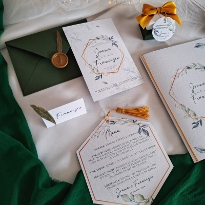 Convites e menus de casamento com design floral em tons verdes e dourados, envelope verde com selo de cera e caixa preta com laço dourado.