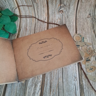 Álbum de fotografias aberto com capa castanha e etiquetas decorativas ao lado numa mesa de madeira