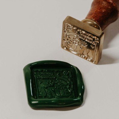 Selo de cera verde com carimbo de madeira e metal em superfície branca