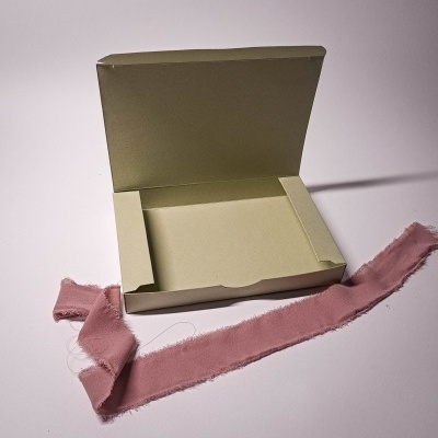 Caixa de cartão creme aberta com fita de tecido rosa ao lado