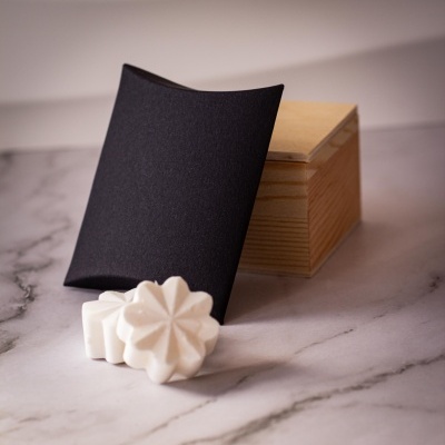 Sabonetes brancos com embalagem preta acolchoada e caixa de madeira sobre superfície de mármore