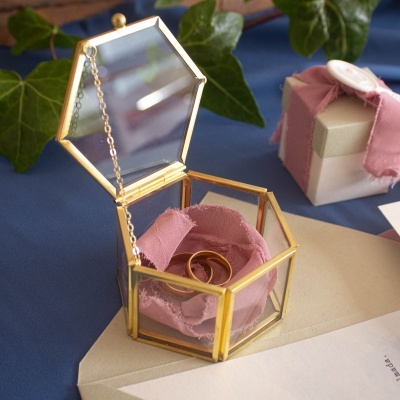 caixa de vidro hexagonal dourada com anéis em tecido rosa