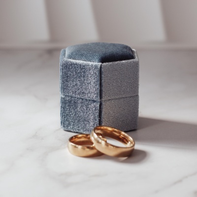 Anéis de ouro com caixa de veludo cinzenta numa superfície branca marmorizada