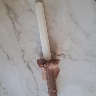 Vela branca com fita castanha em laço sobre mármore cinza claro