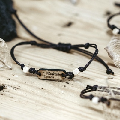 Pulseira com mensagem em placa de madeira e cordão preto sobre madeira clara