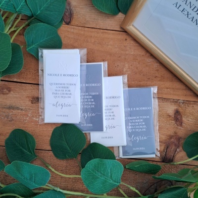 Embalagens transparentes com cartões brancos e cinzentos com texto preto sobre mesa de madeira e folhas verdes artificiais
