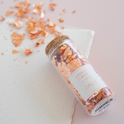 Frasco de vidro com flocos de bronze com brilho cobre num fundo branco