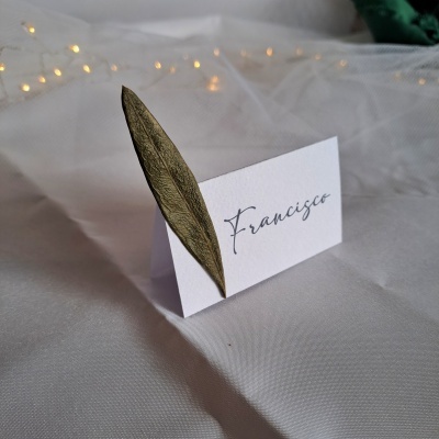 Cartão de lugar branco com nome Francisco e folha seca verde-oliva em tecido branco