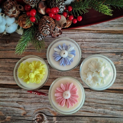 Quatro velas decorativas com flores coloridas em recipientes de vidro sobre mesa de madeira com decoração natural