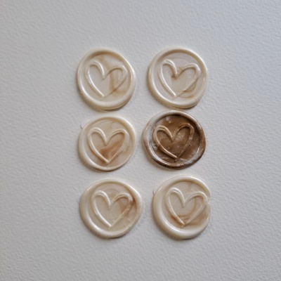 Seis selos de cera redondos com um coração gravado, cinco bege claro e um castanho, sobre fundo branco.