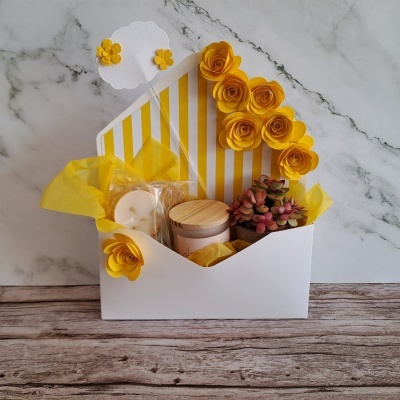 Caixa branca decorada com flores amarelas, vela, planta suculenta e papel de tecido amarelo