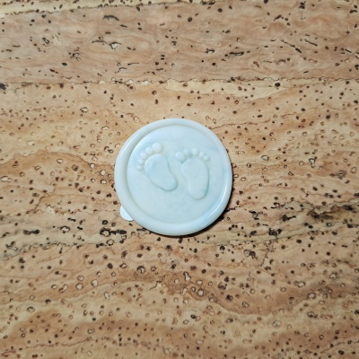 Selo redondo branco com relevo de pezinhos bebés sobre superfície castanha texturada