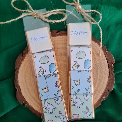 Conjuntos de blocos de madeira decorativos com tema de Páscoa em embalagens transparentes, amarrados com corda, sobre madeira e tecido verde.