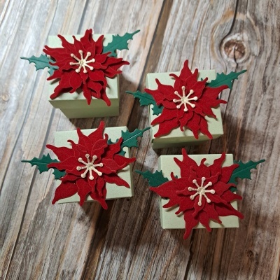 Caixas verdes decoradas com flores vermelhas de tecido e folhas verdes sobre madeira