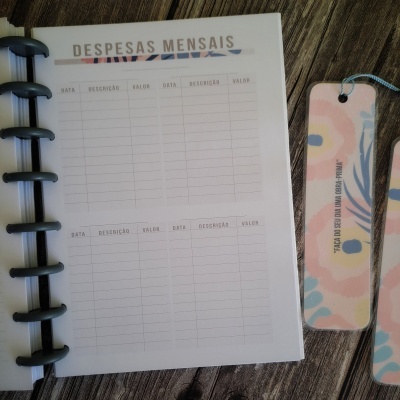 Caderno aberto com página para despesas mensais e dois marcadores de livros florais ao lado